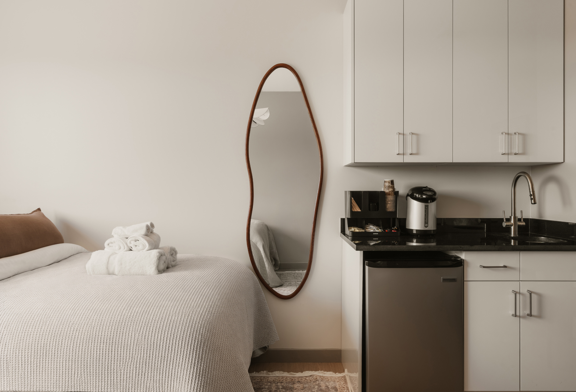Guest bed alongside a kitchenette with mini fridge and coffee maker
