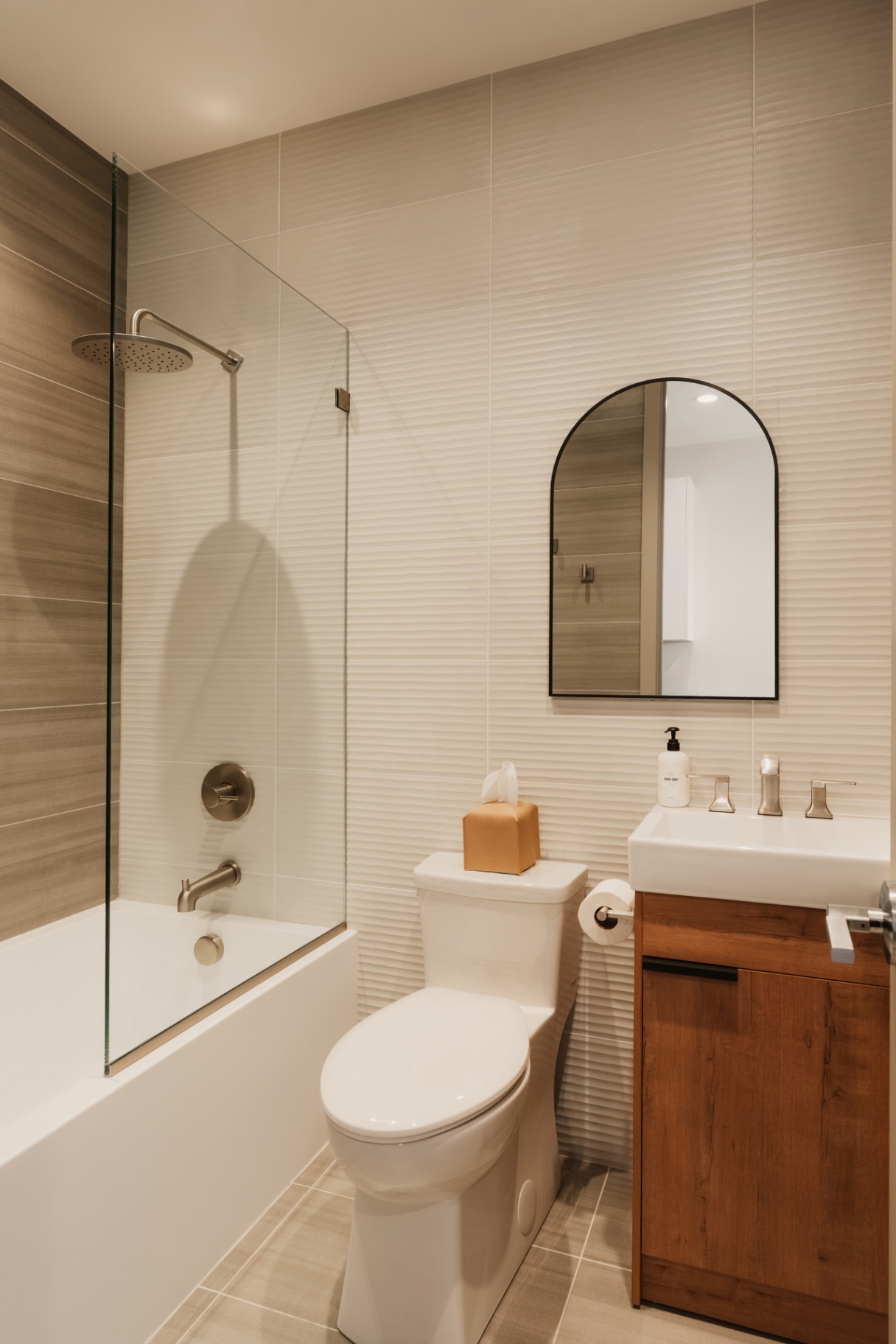 Bathroom with a glass-panelled tub, toilet and wood vanity