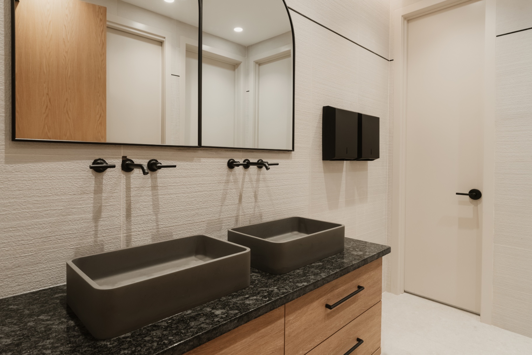 Shared restroom with twin stone vessel sinks on a black granite counter