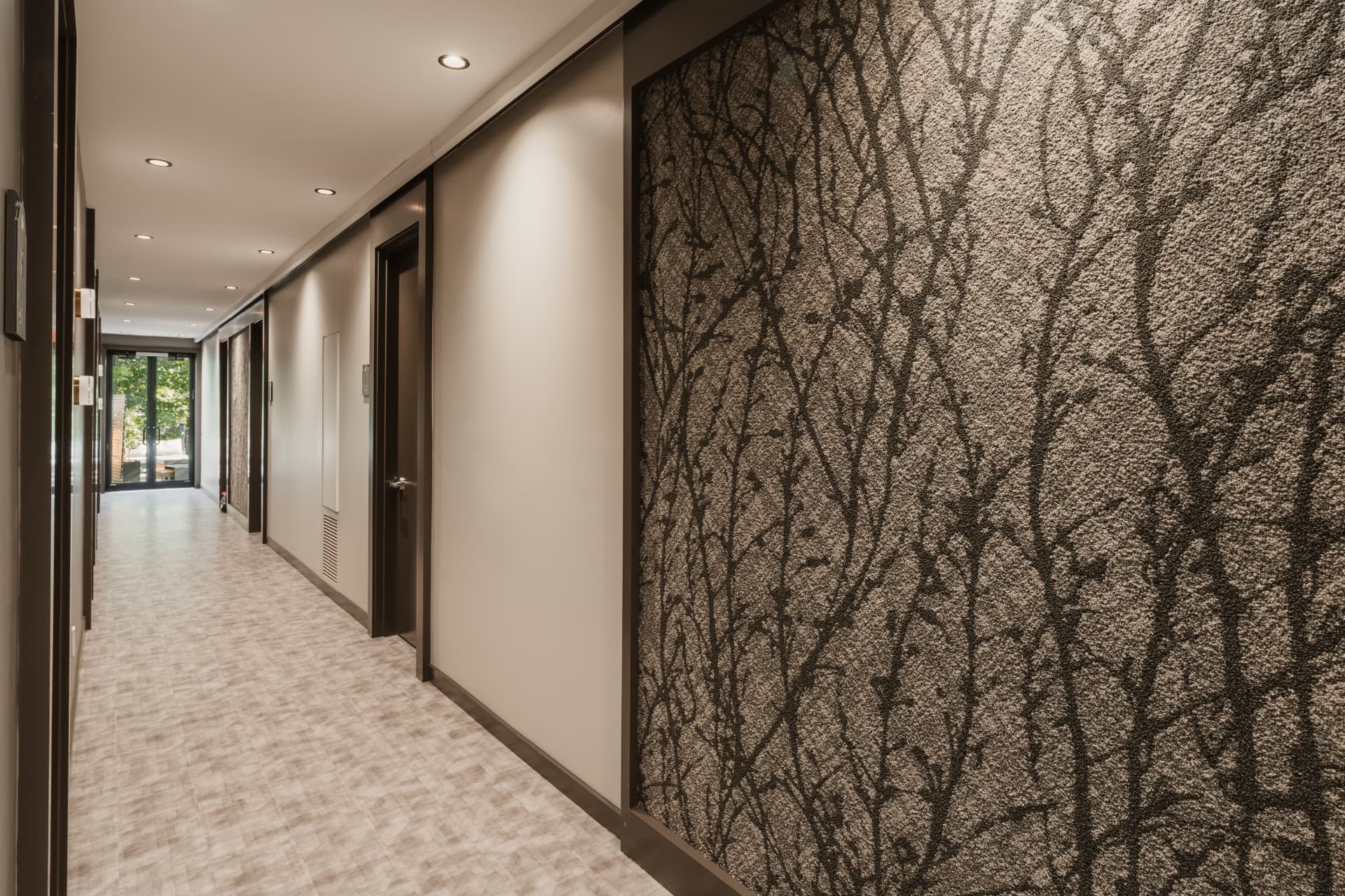 Guest room corridor with tree-patterned wall panels and a glass door opening toward the terrace