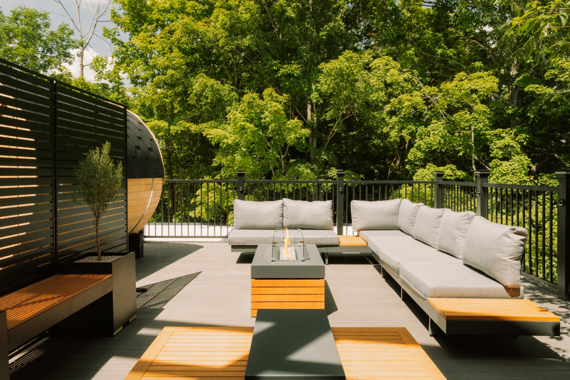Long deck sofa and firepit table framed by black privacy slats and trees