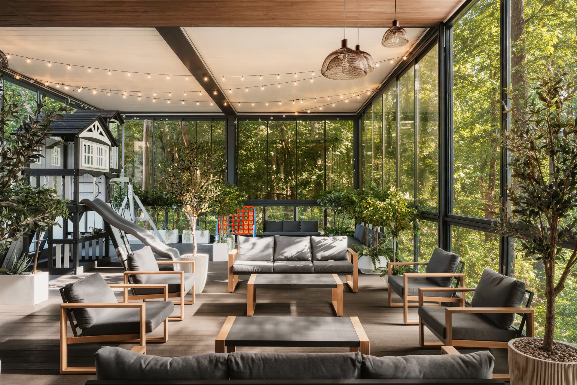 Sunlit glass-enclosed lounge with charcoal seating, string lights and a children's playhouse