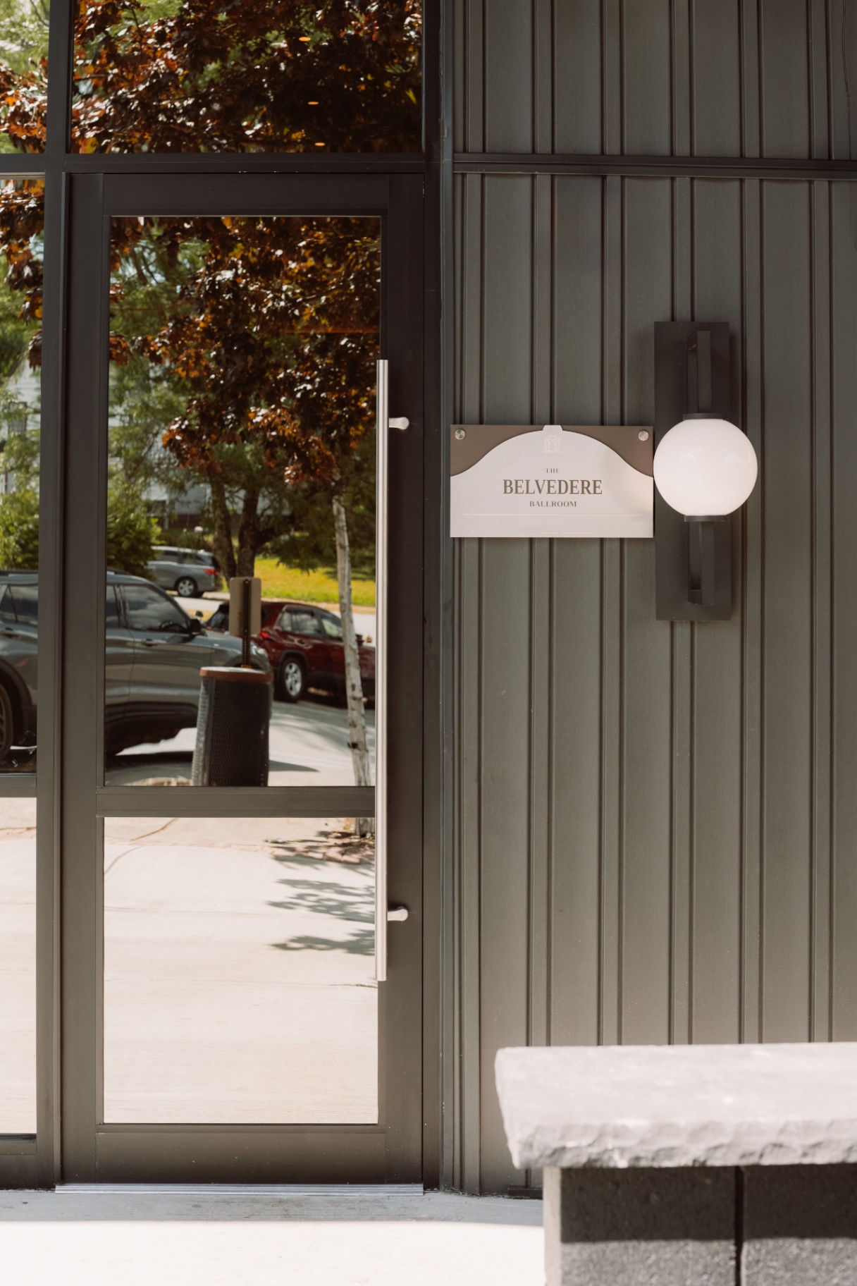 Entrance door of The Belvedere Suites with signage and a stone bench