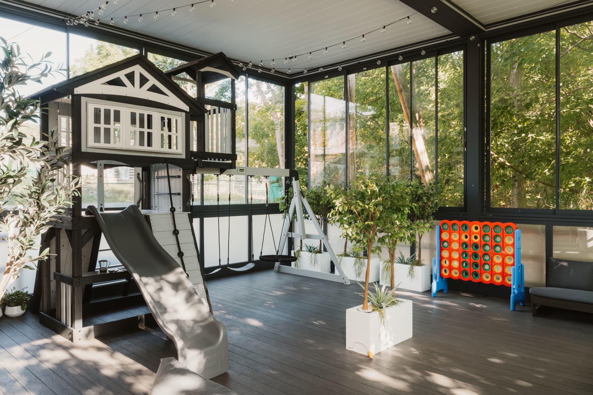 Children's playhouse with a slide and swings beside a giant Connect Four game in the glass terrace