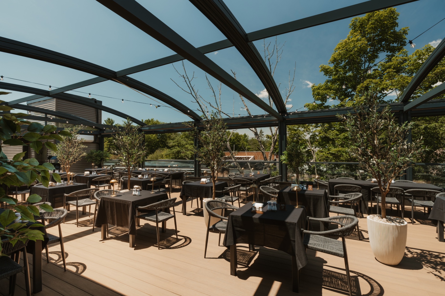 Sunlit glass atrium dining area with woven chairs and dark cafe tables