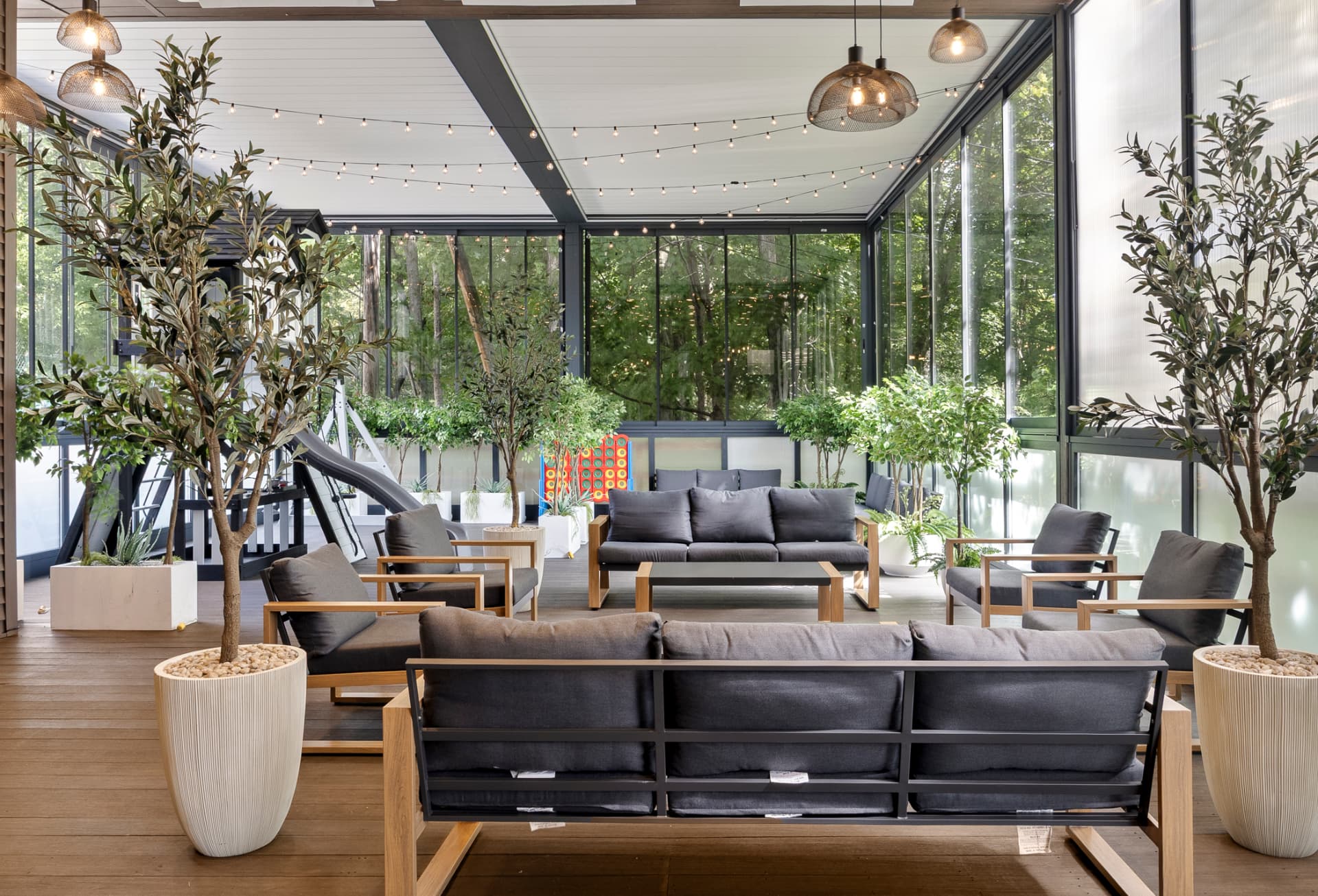 Sunlit glass lounge with deep-cushioned seating and string lights beneath the roof