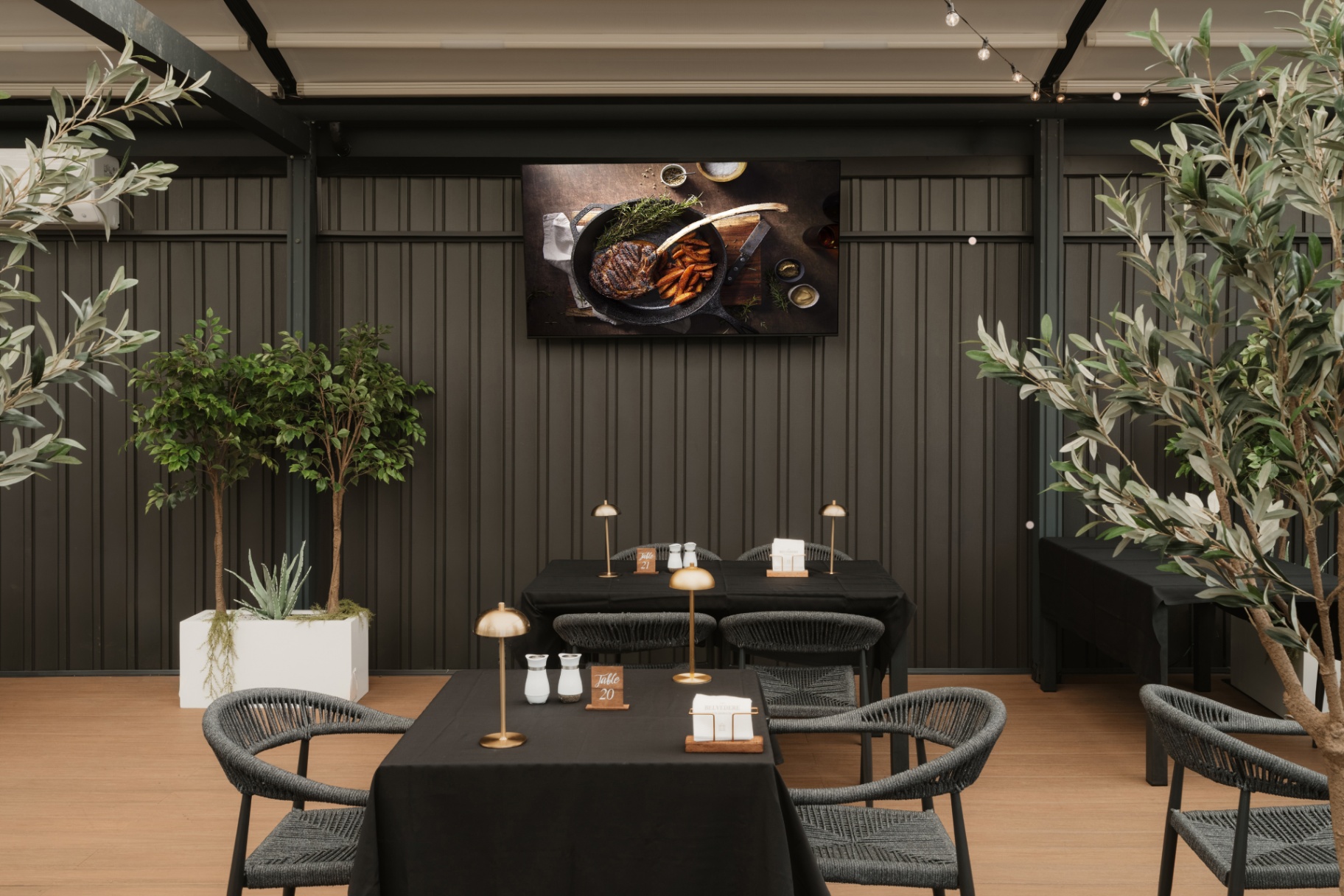 Indoor lounge with olive trees, a wall-mounted screen and intimate seating