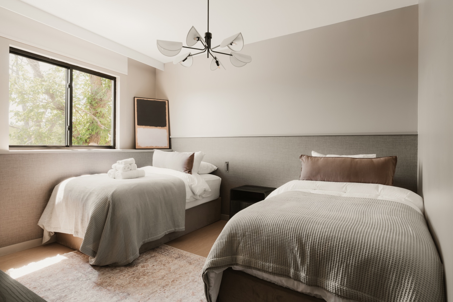 Guest room with two beds and a picture window framing the trees