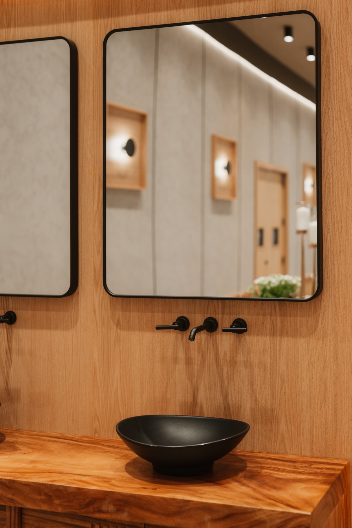Restroom vanity in warm wood with backlit mirrors and a stone basin