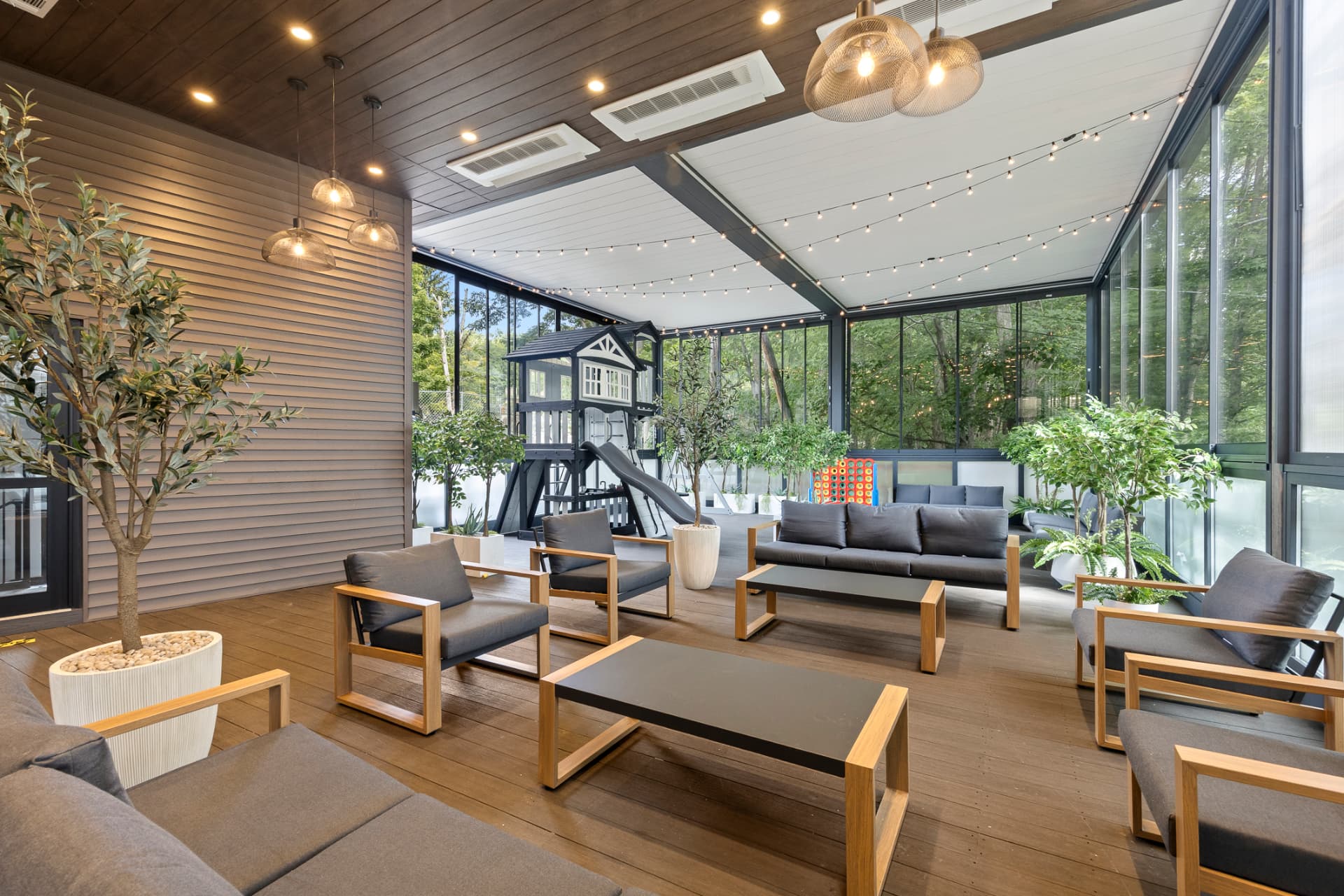 Covered terrace lounge with sofas, armchairs and a children's playhouse by the glass wall