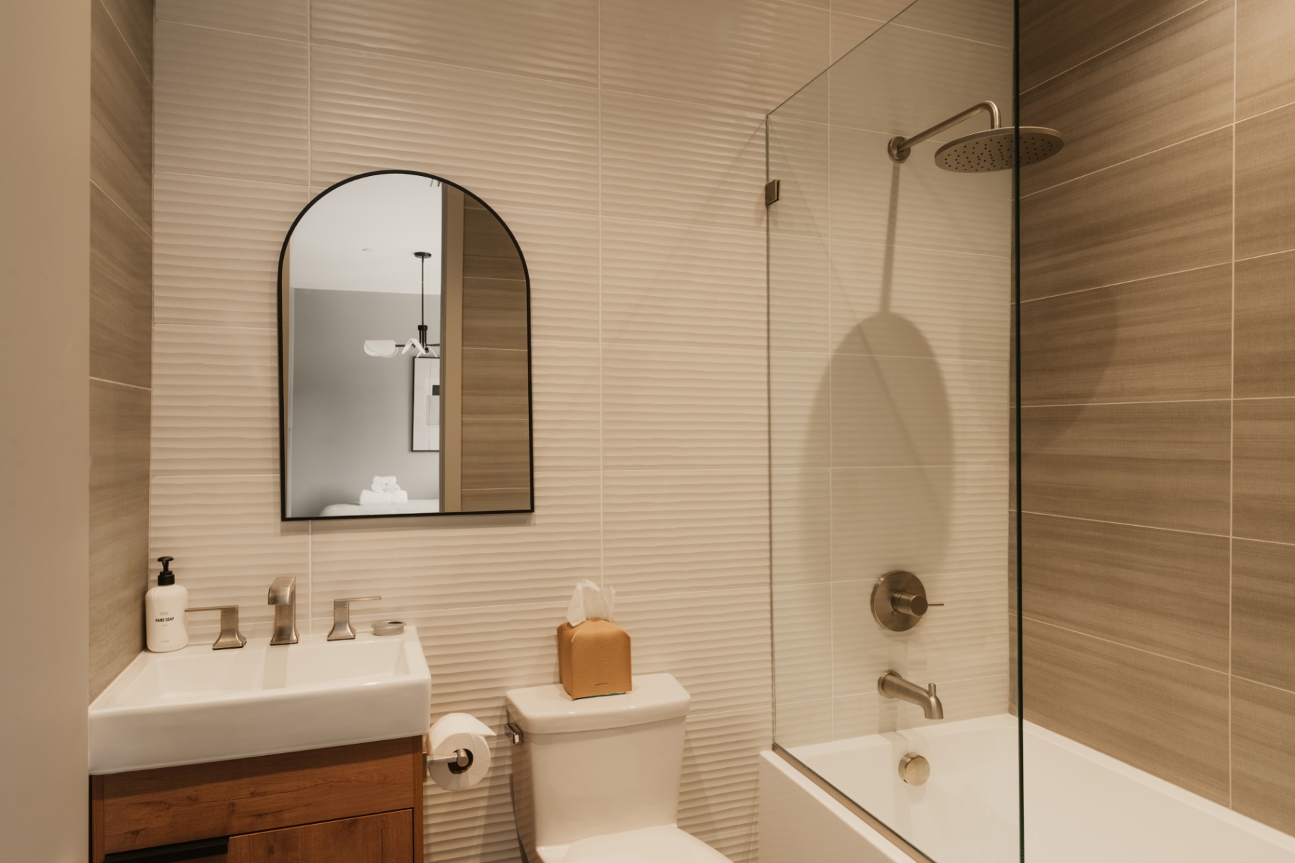 Guest bathroom with a glass shower, arched mirror and wood vanity
